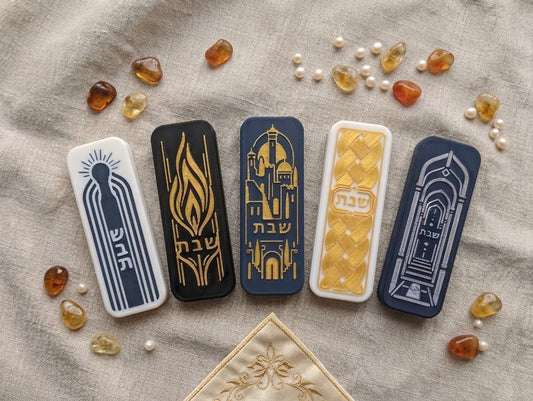 Five Shabbat light switch covers from Atid Judaica laid flat on linen